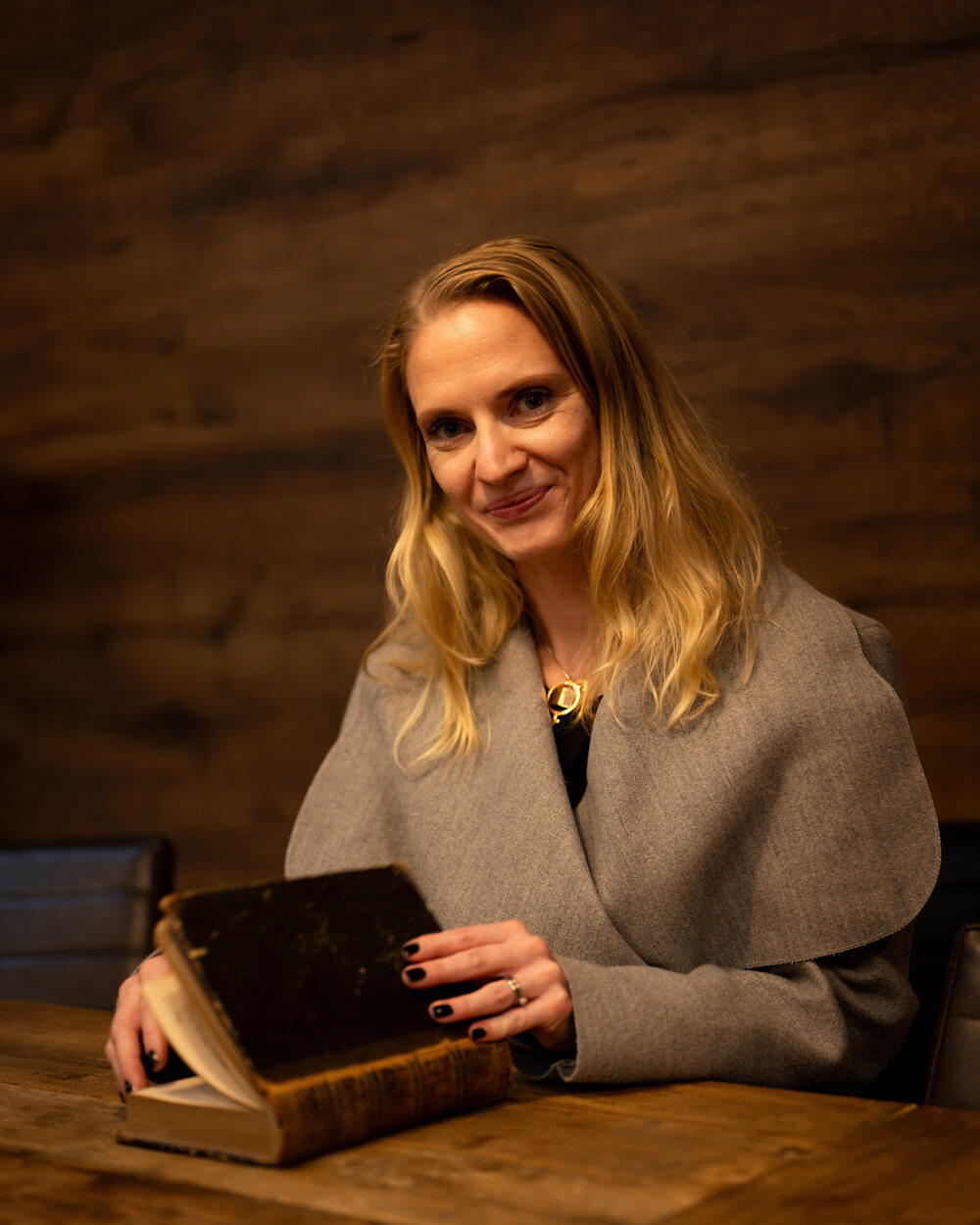 Elisabeth Wadin sitter vid ett bord med en gammal bok framför sig.