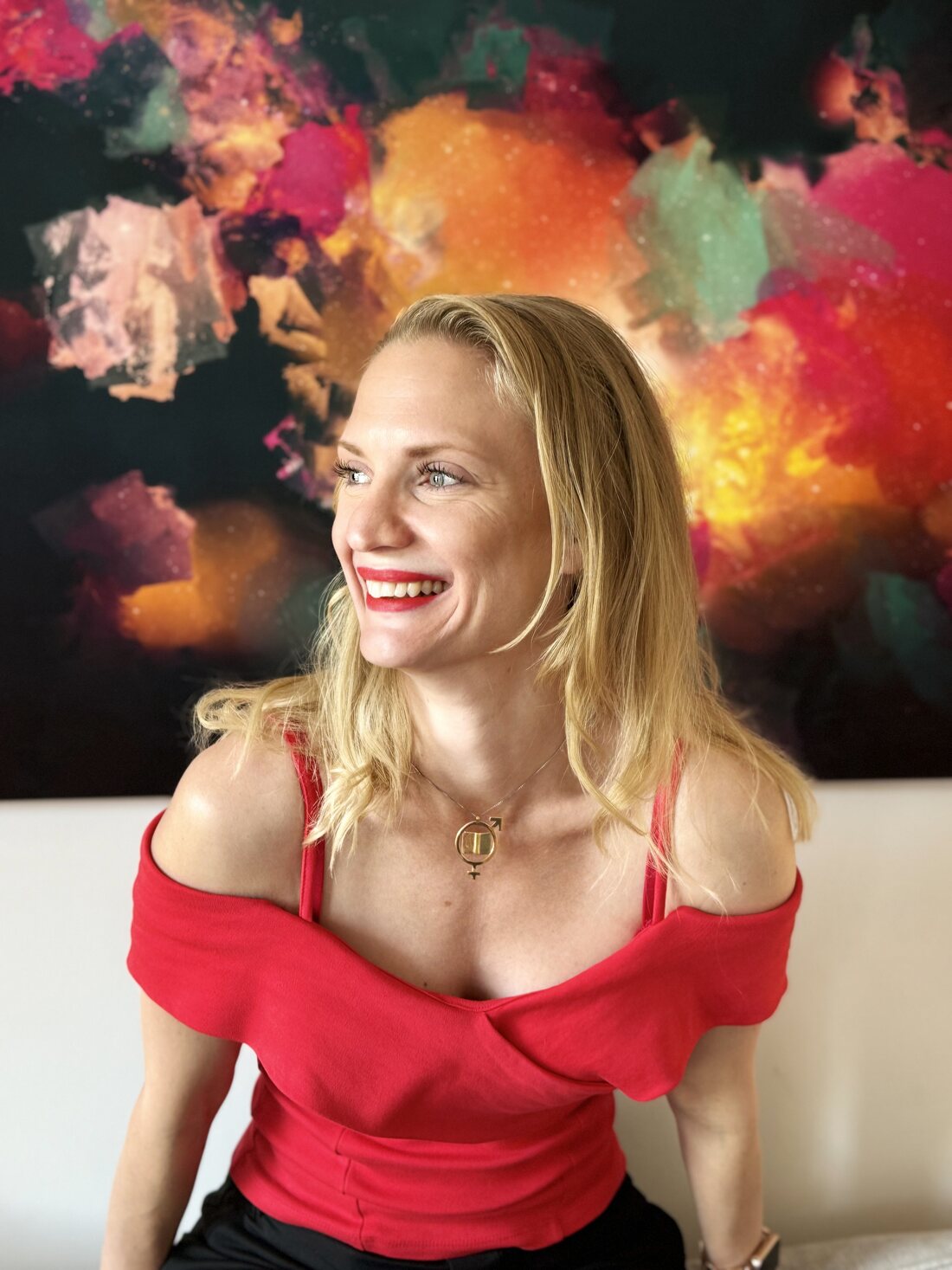 Elisabeth Wadin skrattar och tittar åt sidan, framför en stor färgstark målning.
