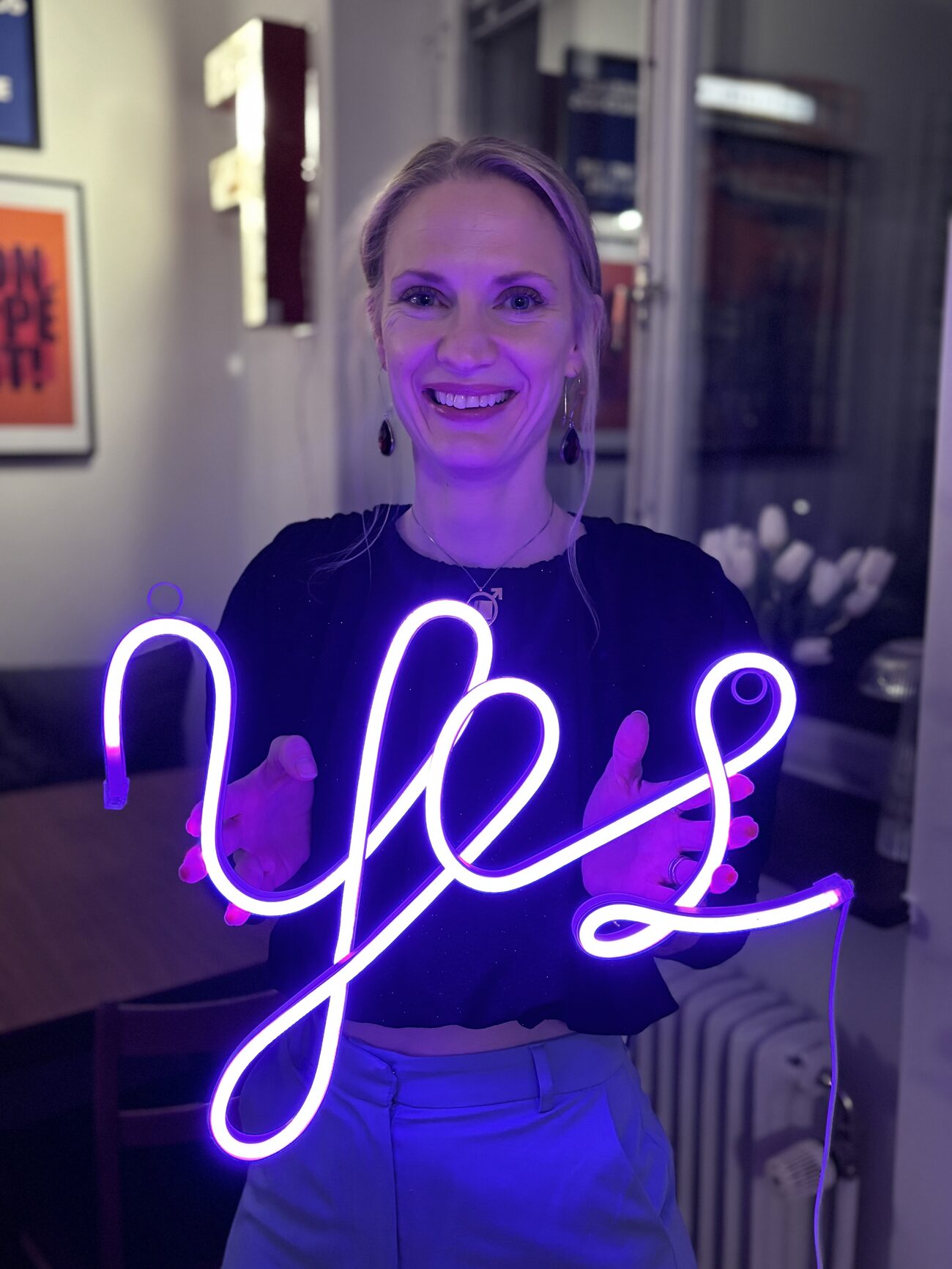Elisabeth Wadin bredvid en neonskylt som lyser ordet Yes.